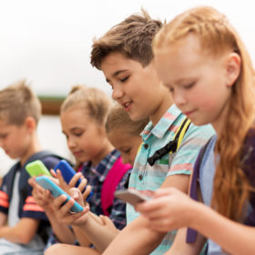 Απεικονίζεται μια όμορφη παιδική παρέα από αγοράκια και κοριτσάκια που έχουν όλα στραμμένη την προσοχή τους στα κινητά τηλέφωνα τους.